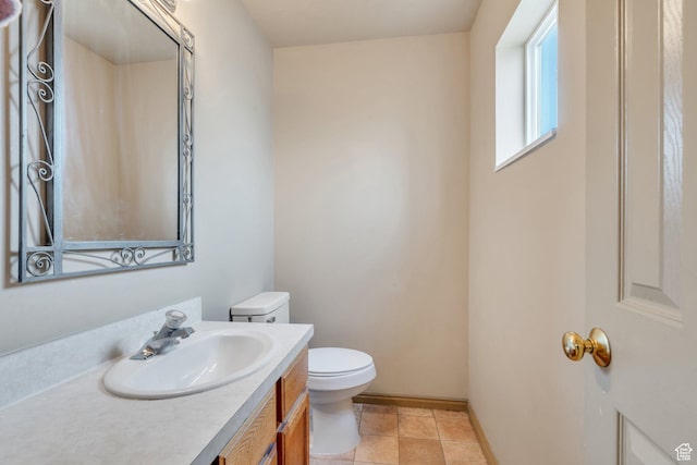 half bathroom with toilet, baseboards, vanity, and tile patterned floors