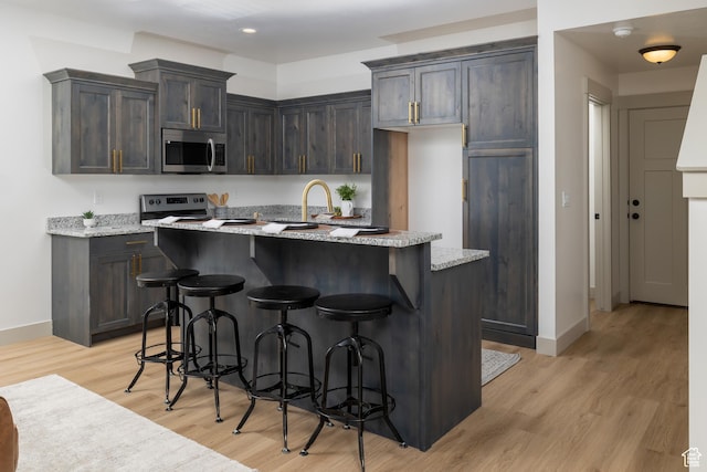 856 E 250 N, Hyrum, UT 84319 - kitchen featuring appliances with stainless steel finishes, baseboards, light wood-style flooring, a breakfast bar area, and light stone countertops
