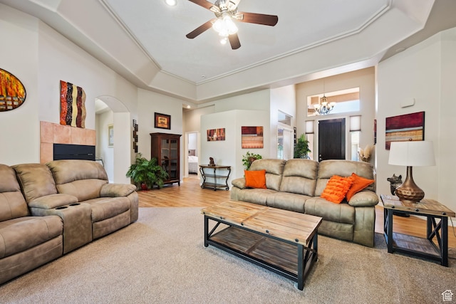 carpeted living area featuring ceiling fan, a high ceiling, a chandelier, arched walkways, and a fireplace
