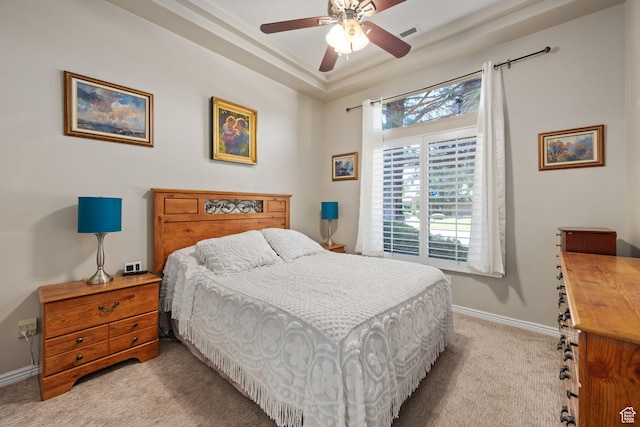 bedroom featuring light carpet, baseboards, ceiling fan, and a raised ceiling