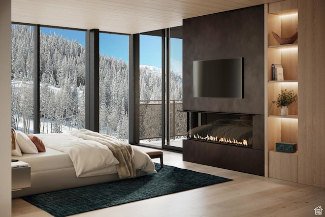 bedroom with expansive windows, wood finished floors, multiple windows, and a warm lit fireplace