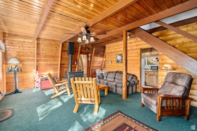 sitting room with a wood stove, beam ceiling, carpet, wooden walls, and ceiling fan