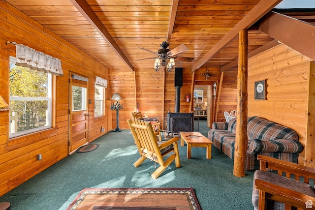 living area with a wood stove, carpet floors, wooden walls, ceiling fan, and wood ceiling