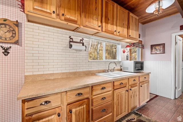 kitchen with stainless steel microwave, wallpapered walls, wood ceiling, a sink, and light countertops