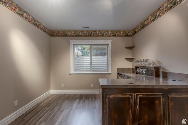kitchen featuring dark wood finished floors, dark brown cabinets, baseboards, dark countertops, and a peninsula