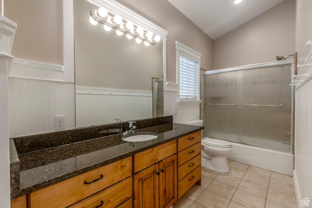 bathroom with a wainscoted wall, tile patterned flooring, vanity, toilet, and enclosed tub / shower combo