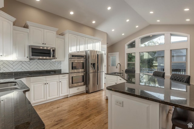 kitchen with stainless steel appliances, a sink, white cabinets, backsplash, and lofted ceiling