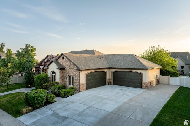french country style house with stone siding, concrete driveway, an attached garage, stucco siding, and roof with shingles