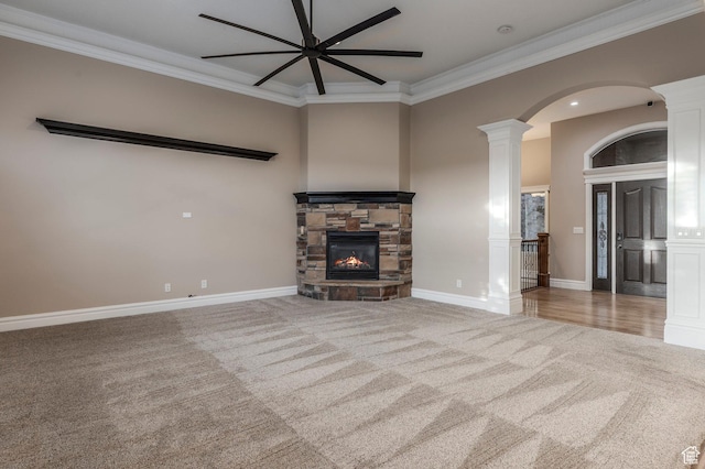 unfurnished living room with carpet flooring, a ceiling fan, ornamental molding, a fireplace, and decorative columns