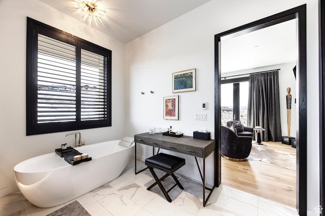full bathroom featuring marble finish floors, a freestanding bath, and baseboards