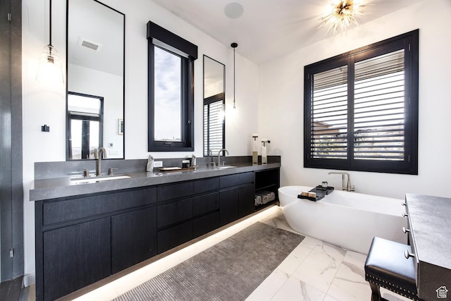 full bath with marble look tile flooring, healthy amount of natural light, a freestanding bath, and double vanity