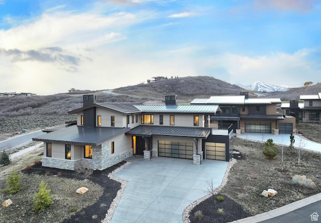 contemporary home featuring stone siding, a mountain view, concrete driveway, metal roof, and a standing seam roof