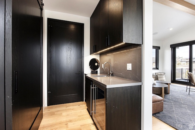 kitchen with a sink, wine cooler, light countertops, light wood-style floors, and lofted ceiling