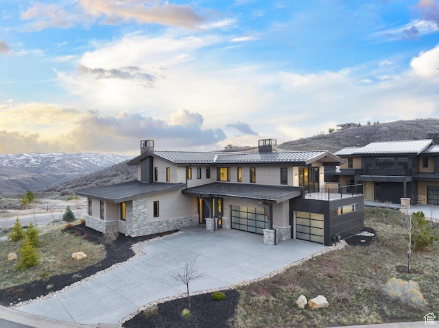 view of front of home with stone siding, a chimney, a garage, concrete driveway, and a standing seam roof