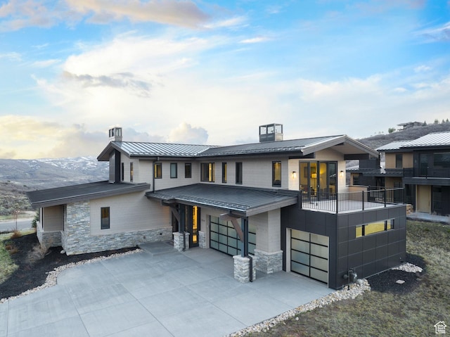 contemporary home featuring a standing seam roof, stone siding, an attached garage, metal roof, and a balcony