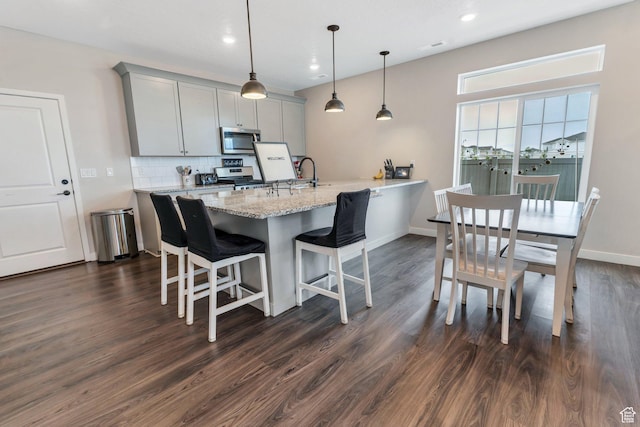 24 S Baker Spring Cv, Saratoga Springs, UT 84045 - kitchen featuring appliances with stainless steel finishes, gray cabinets, a breakfast bar area, dark wood-style floors, and decorative backsplash