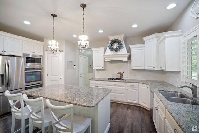 kitchen with appliances with stainless steel finishes, a sink, a kitchen island, a chandelier, and light stone countertops