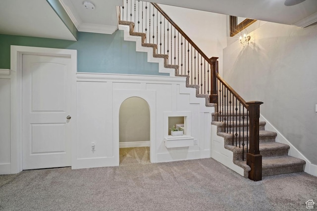 stairs with carpet flooring, crown molding, and a decorative wall
