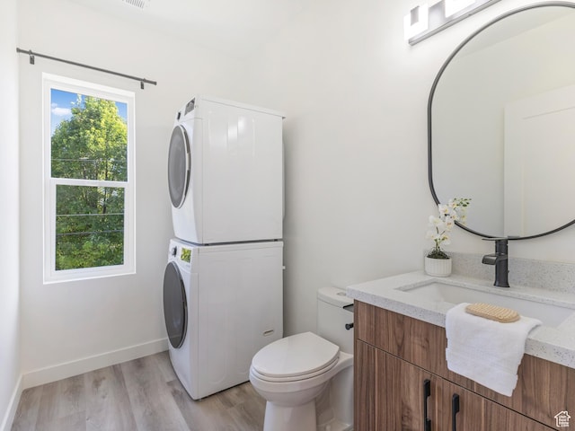 half bathroom with stacked washer / dryer, wood finished floors, toilet, vanity, and baseboards
