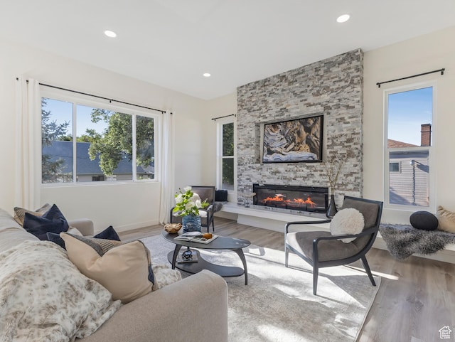 living room featuring wood finished floors, a stone fireplace, recessed lighting, and baseboards