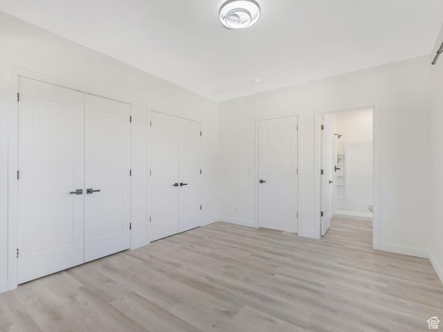 unfurnished bedroom with multiple closets, light wood-style flooring, baseboards, and ensuite bath
