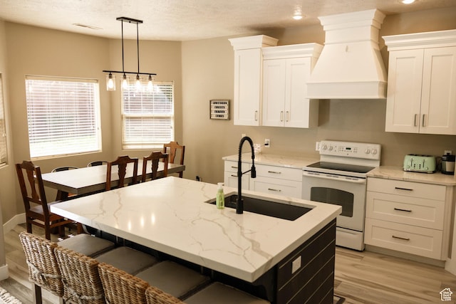 kitchen with white electric range oven, premium range hood, a sink, light wood-style flooring, and white cabinets