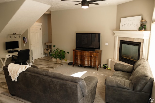living area with ceiling fan, wood finished floors, a tile fireplace, and baseboards