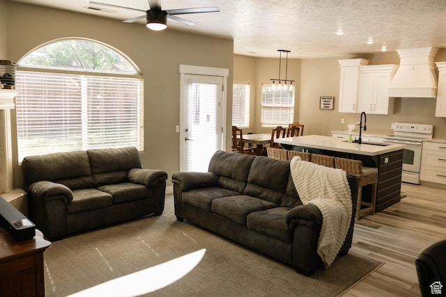 living area featuring ceiling fan, light wood-style flooring, and a textured ceiling