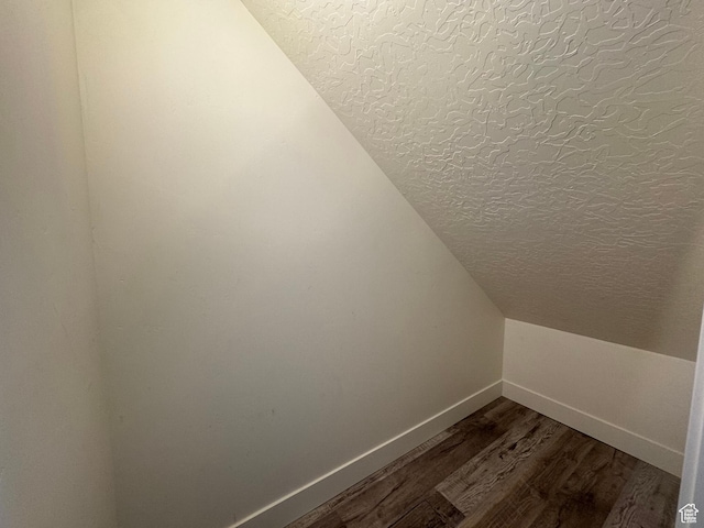 additional living space featuring a textured ceiling, lofted ceiling, baseboards, and dark wood finished floors