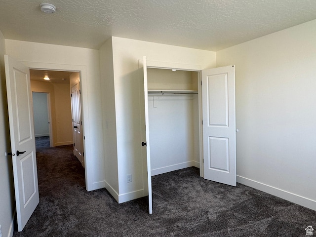 unfurnished bedroom with dark colored carpet, baseboards, a closet, and a textured ceiling