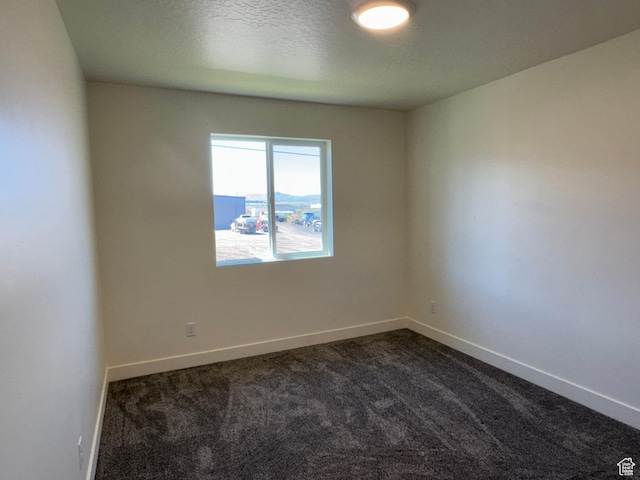 empty room featuring dark colored carpet and baseboards