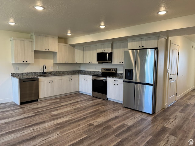 kitchen with appliances with stainless steel finishes, dark wood-type flooring, a sink, baseboards, and a textured ceiling