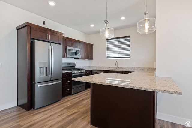 kitchen featuring stainless steel appliances, a peninsula, dark brown cabinets, decorative light fixtures, and light wood-type flooring