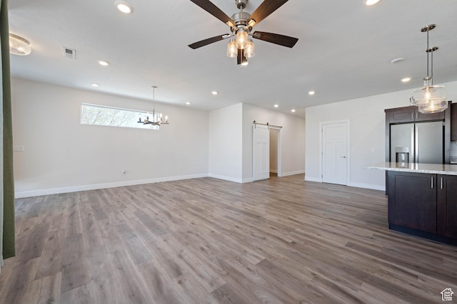 unfurnished living room with a barn door, recessed lighting, wood finished floors, a ceiling fan, and baseboards