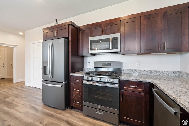 kitchen featuring appliances with stainless steel finishes, light wood-style flooring, dark brown cabinetry, light stone countertops, and recessed lighting