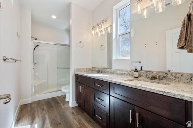 bathroom with wood finished floors, a shower stall, toilet, double vanity, and baseboards