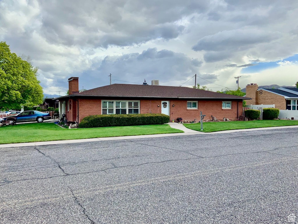ranch-style house with a chimney, a front yard, and brick siding