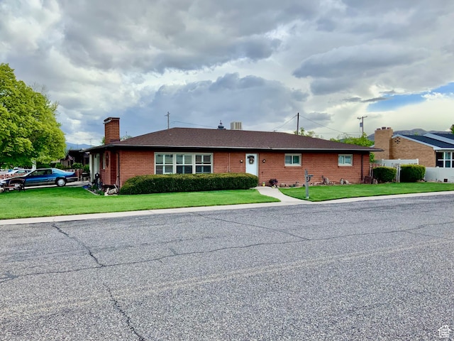 ranch-style house with a chimney, a front yard, and brick siding