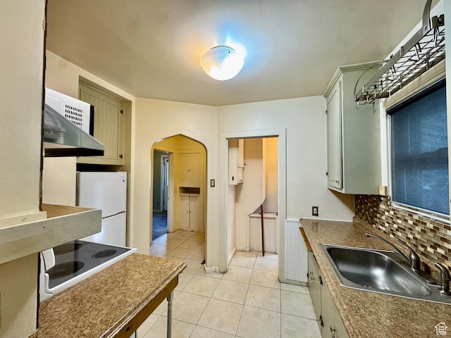 kitchen featuring freestanding refrigerator, arched walkways, a sink, cooktop, and light tile patterned floors
