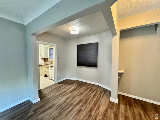 unfurnished room with a textured ceiling, wood finished floors, and baseboards