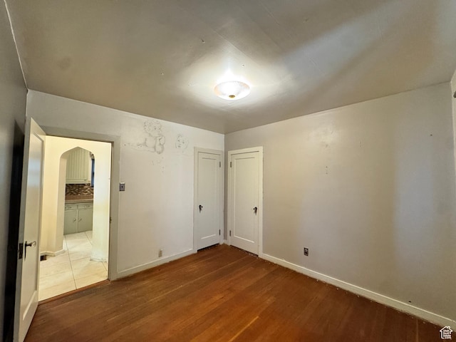 unfurnished bedroom with arched walkways, wood finished floors, and baseboards
