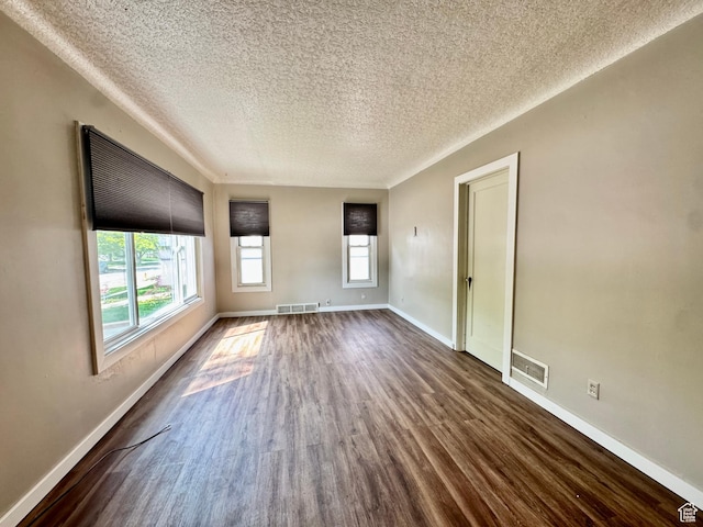 unfurnished room with a textured ceiling, dark wood finished floors, and baseboards