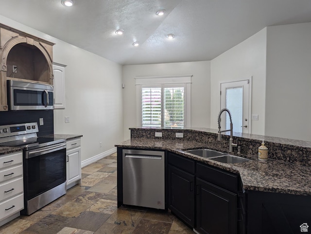 kitchen with stainless steel appliances, a sink, stone tile flooring, dark stone counters, and a textured ceiling