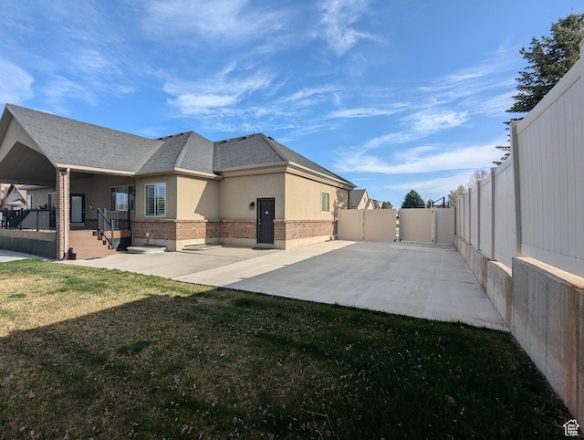 back of house featuring a gate, stucco siding, covered porch, and brick siding