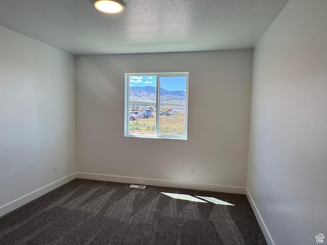 spare room with dark colored carpet, a textured ceiling, and baseboards