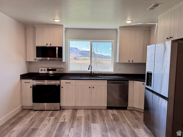 kitchen with stainless steel appliances, a sink, dark countertops, light wood-style flooring, and a textured ceiling