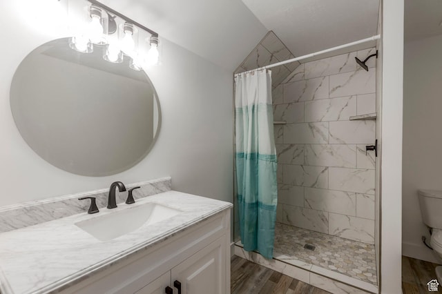 full bath featuring toilet, a tile shower, lofted ceiling, vanity, and wood finished floors