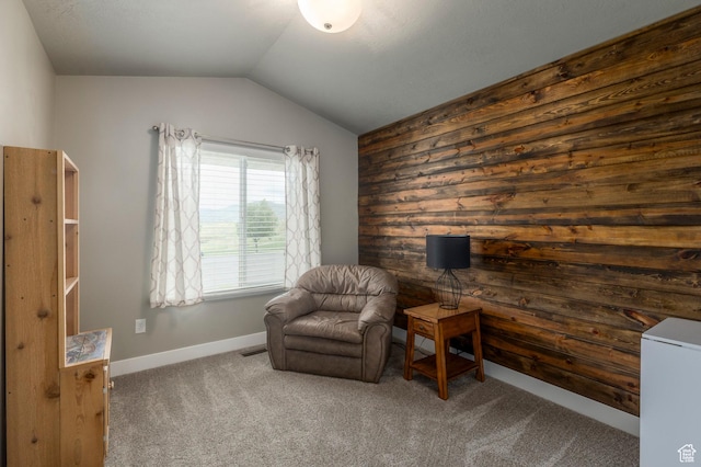 sitting room featuring carpet flooring, vaulted ceiling, wood walls, and baseboards