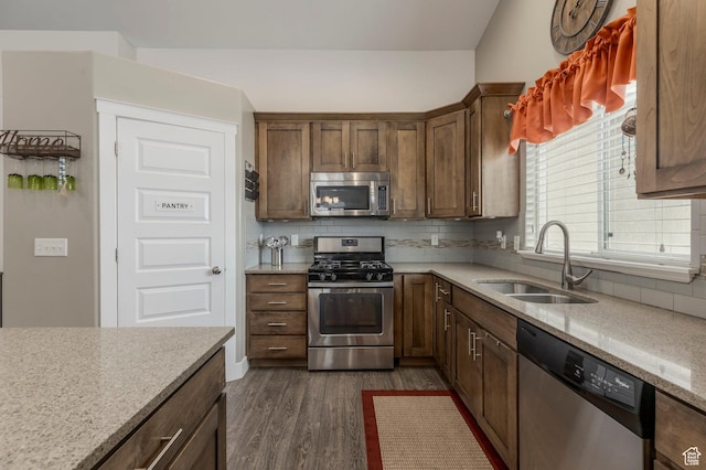 kitchen featuring appliances with stainless steel finishes, a sink, dark wood finished floors, backsplash, and light stone countertops