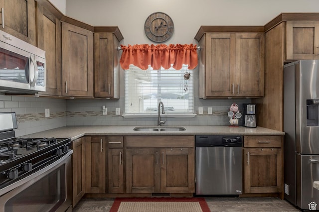 kitchen with stainless steel appliances, a sink, backsplash, and wood finished floors
